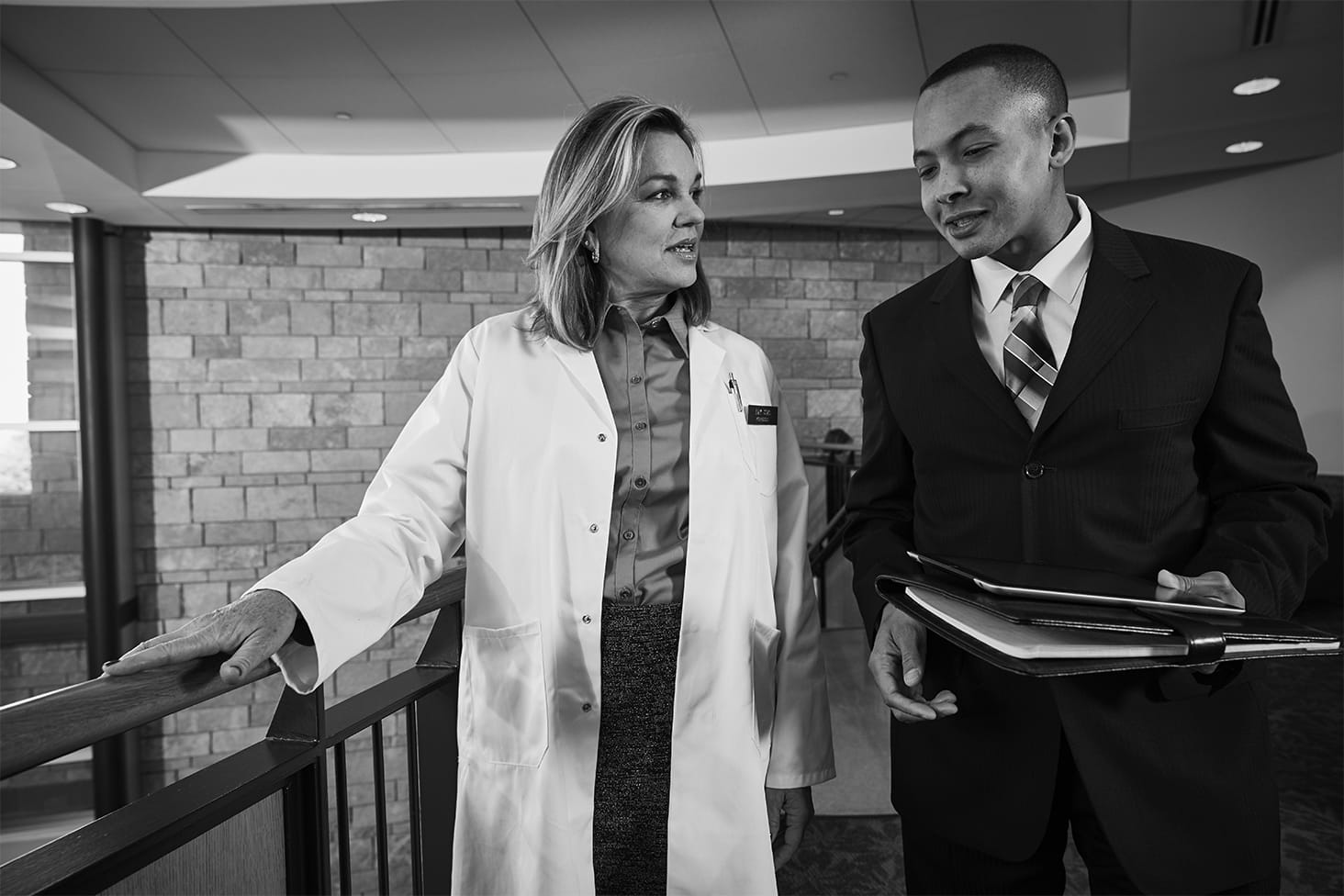 Female doctor speaks with a male representative in a hallway.