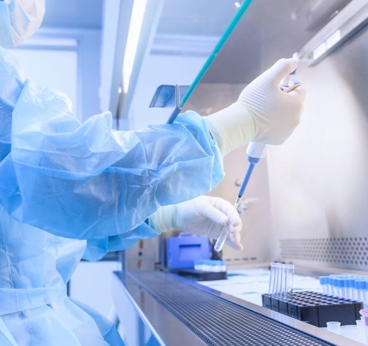 Technician in full lab suit, using testing equipment